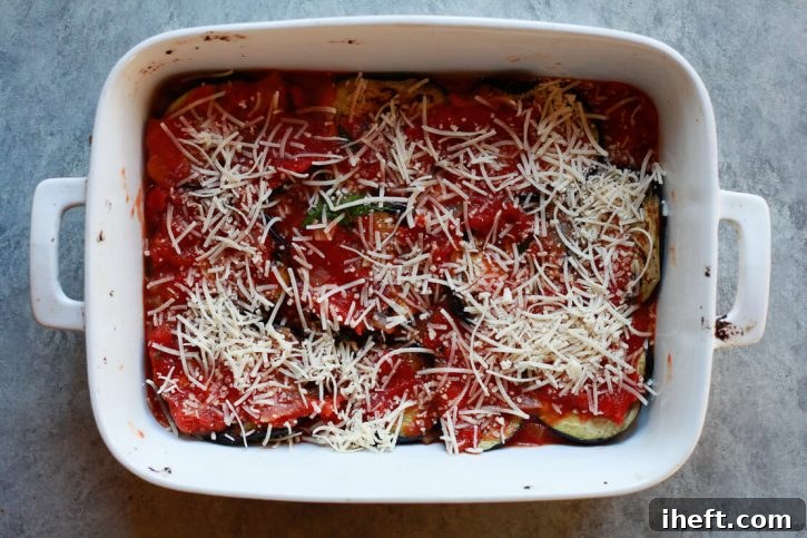 A white casserole dish topped layered with eggplant, tomato sauce, and vegan parmesan. 