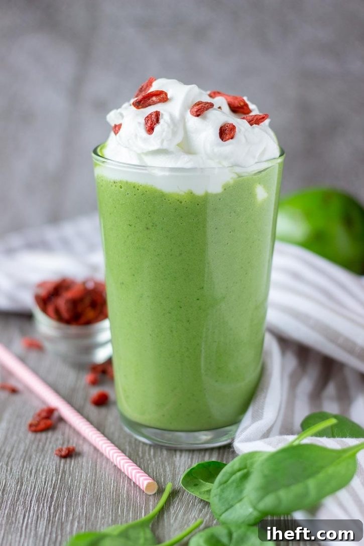 Green matcha smoothie topped with whipped cream and goji berries in a tall glass.