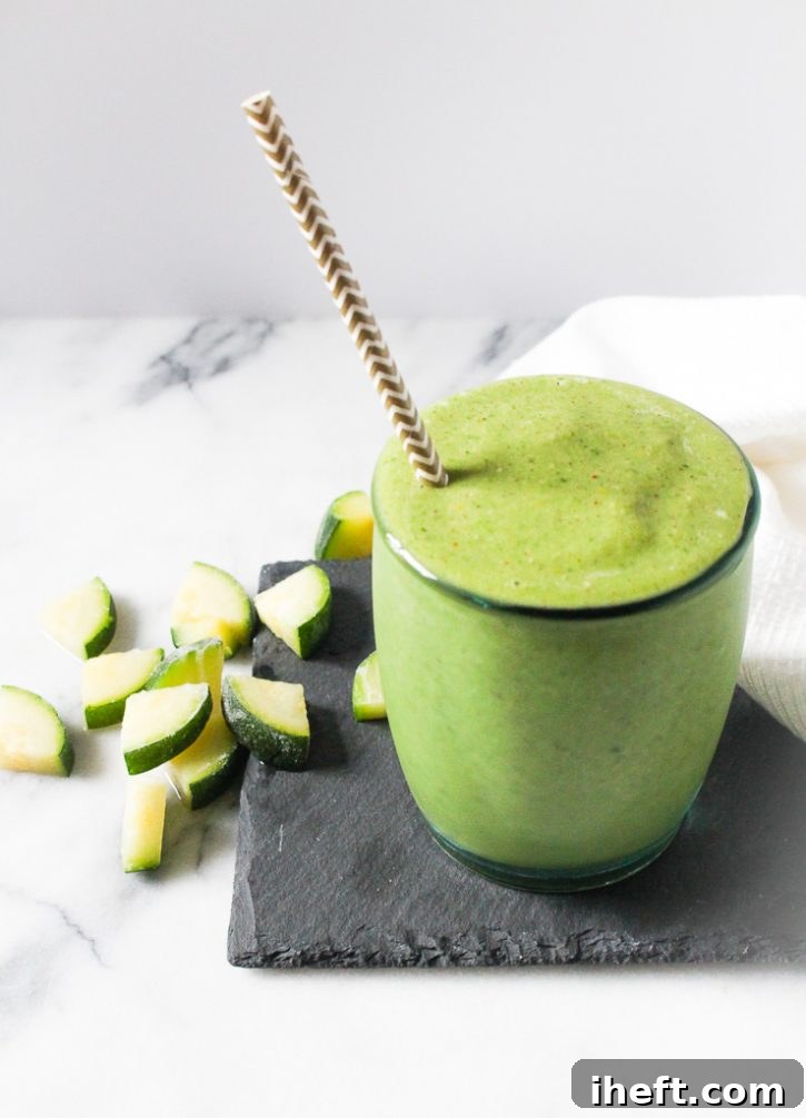 Green smoothie with a straw and chopped zucchini in the background.