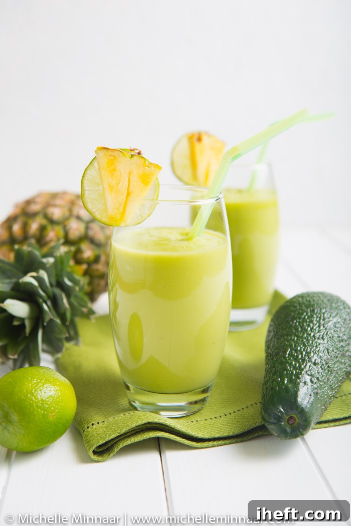 Two glasses filled with a pineapple avocado green smoothie and garnished with pineapple wedges.