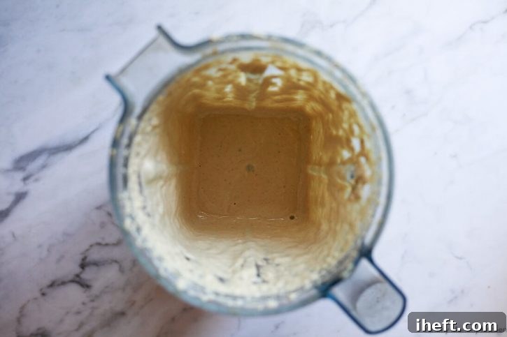 A high-speed Vitamix blender, now filled with the fully blended creamy vegan Caesar dressing, showcases its smooth and luscious texture. The dressing swirls enticingly, indicating its perfect consistency and readiness for use. This image captures the delicious outcome of the blending process.