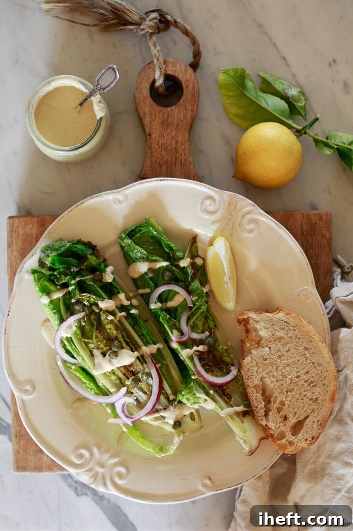 Two perfectly grilled Romaine Caesar salad hearts are beautifully arranged on a pristine white plate, generously drizzled with rich vegan Caesar dressing. The vibrant green lettuce is elegantly garnished with a sprinkle of briny capers and thinly sliced red onions, creating an inviting and gourmet presentation.