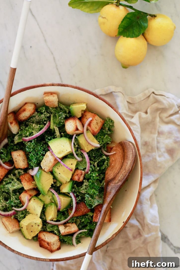 A beautifully composed bowl of vibrant vegan kale Caesar salad, featuring creamy avocado slices, rustic sourdough croutons, and delicate red onion, is presented invitingly. The rich colors and textures highlight a delicious and healthy plant-based meal, perfectly dressed with our homemade vegan Caesar.
