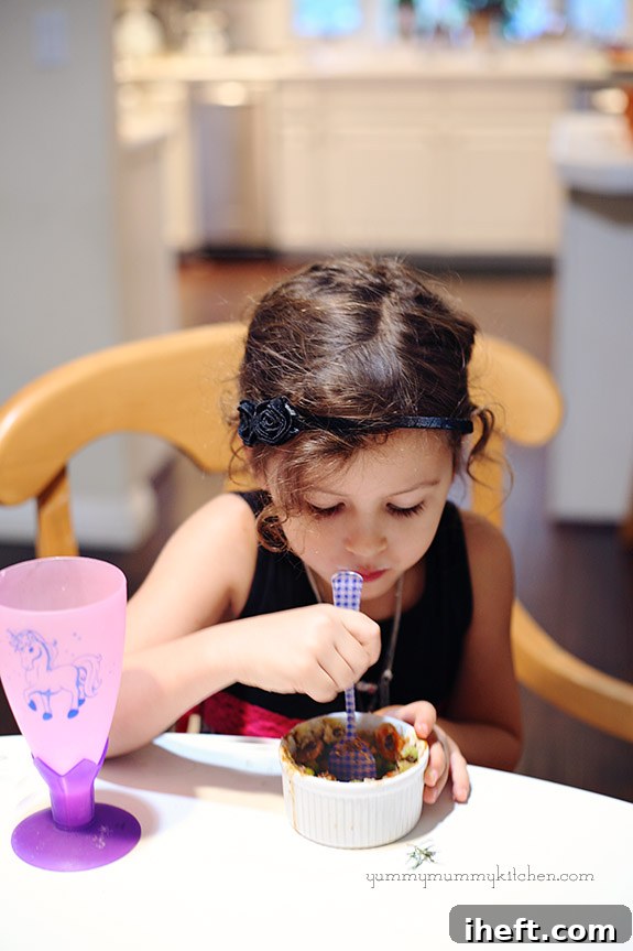 A young girl happily eating an individual bowl of lentil shepherd's pie, enjoying the comforting and healthy meal.