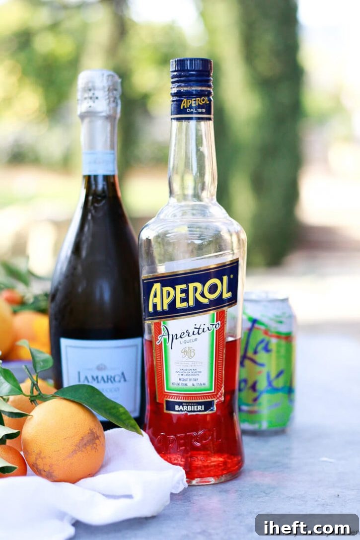 A bottle of Aperol and a bottle of Prosecco are placed on a table with fresh oranges in the background.