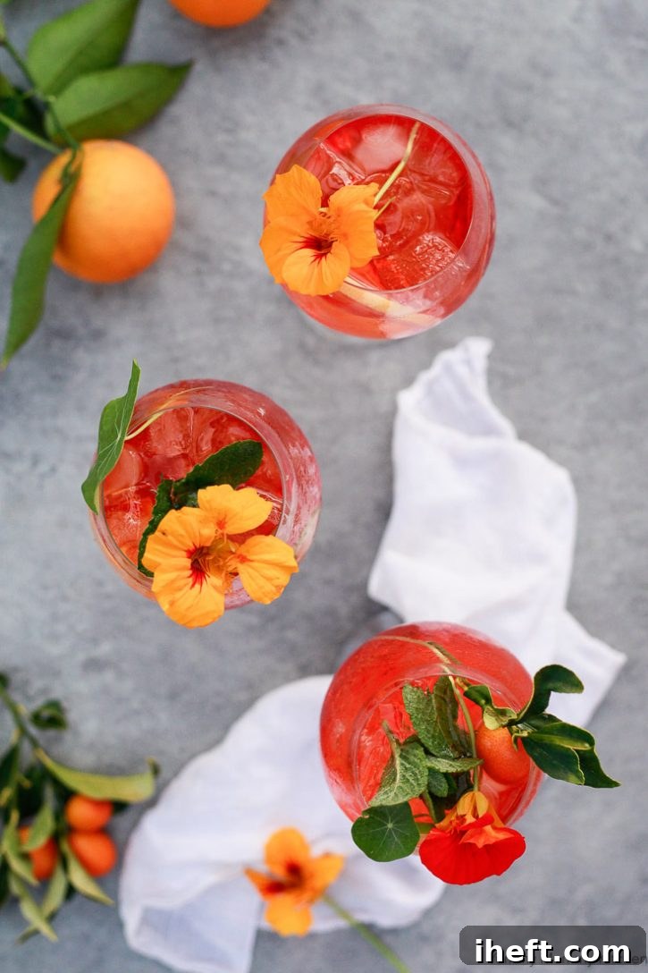 Three Italian Aperol Spritz cocktails, garnished with nasturtium flowers, sit on an outdoor table.