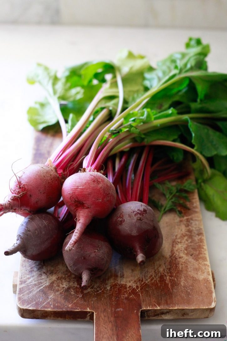 A bunch of beets with beet greens on a wooden cutting board on a marble countertop. 