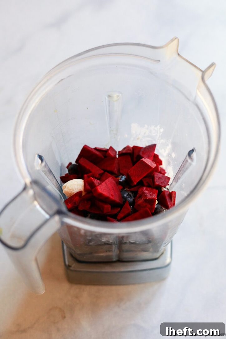 Blueberries, banana, and raw beets in a Vitamix blender on a white countertop. 