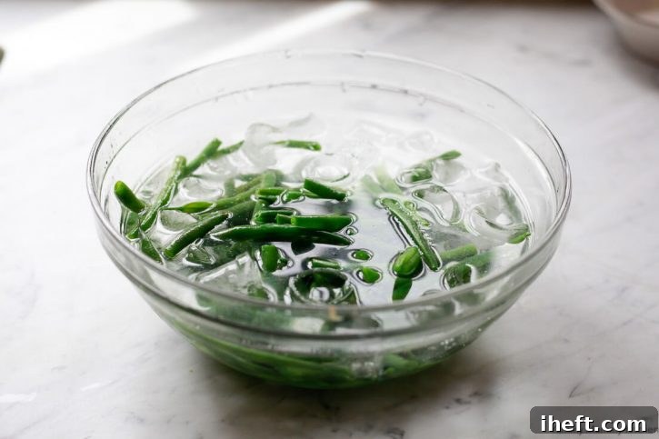 Cooked green beans in a bowl of ice water on a marble counter. 