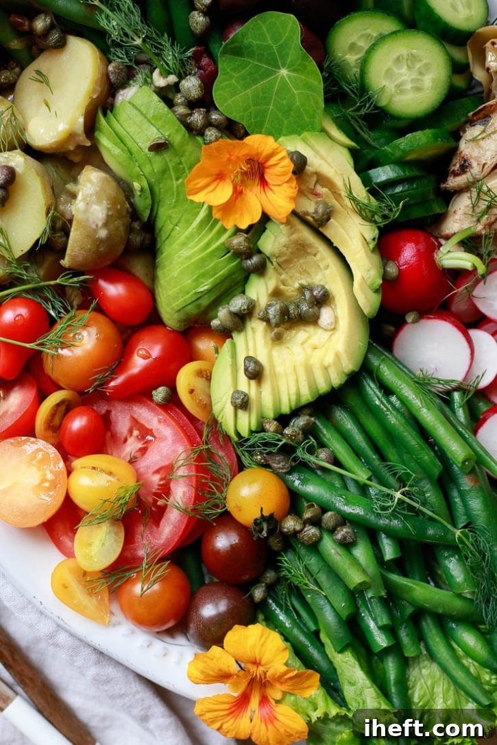 Close-up food photography of Nicoise salad with avocado, tomato, capers, green beans, and potatoes. 