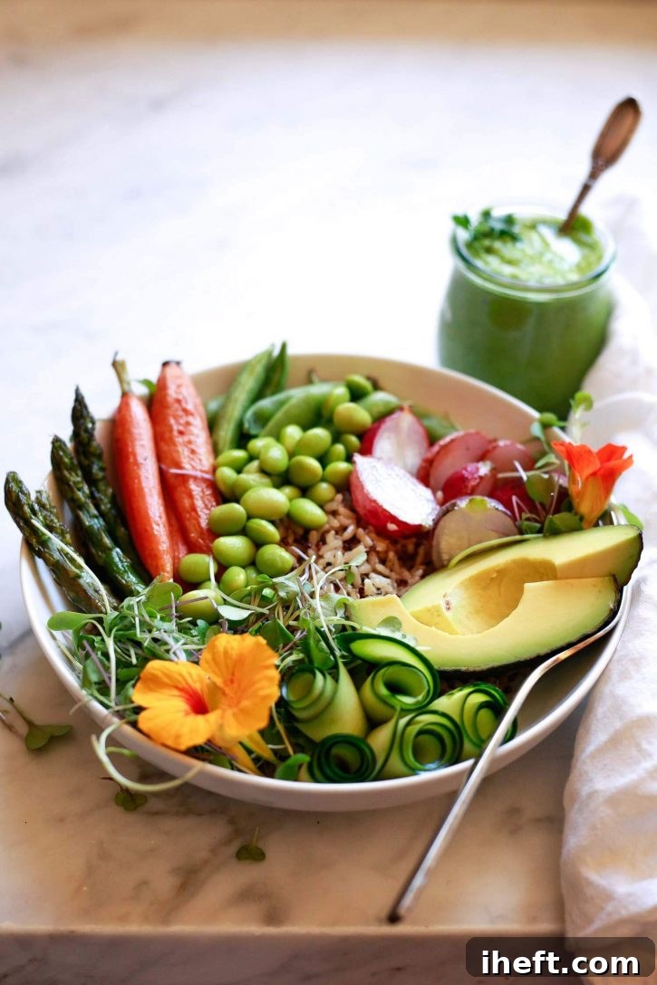 A beautifully composed vegan brown rice and quinoa grain bowl, generously packed with a colorful array of roasted and fresh vegetables, is artfully arranged with a separate side bowl of vibrant green goddess dressing, inviting a delicious and healthy meal.