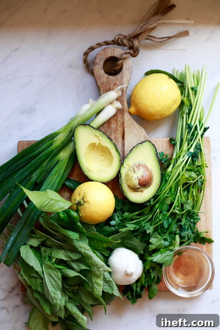 Essential ingredients for crafting a homemade vegan avocado Green Goddess dressing, including a ripe avocado, fresh lemon, a generous bunch of aromatic herbs, and a bottle of apple cider vinegar, are thoughtfully arranged on a pristine countertop, ready for blending.