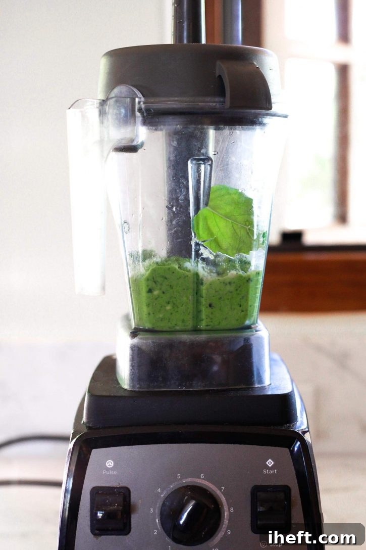 The vibrant green avocado Green Goddess dressing is in the process of blending smoothly within a Vitamix blender, creating a creamy and homogenous consistency, ready to be enjoyed.