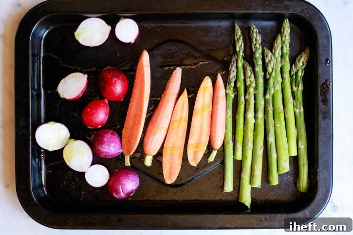 A colorful assortment of fresh radishes, slender carrots, and vibrant asparagus spears are neatly arranged on a roasting sheet, lightly coated with olive oil and seasoned, poised for roasting to bring out their natural sweetness.