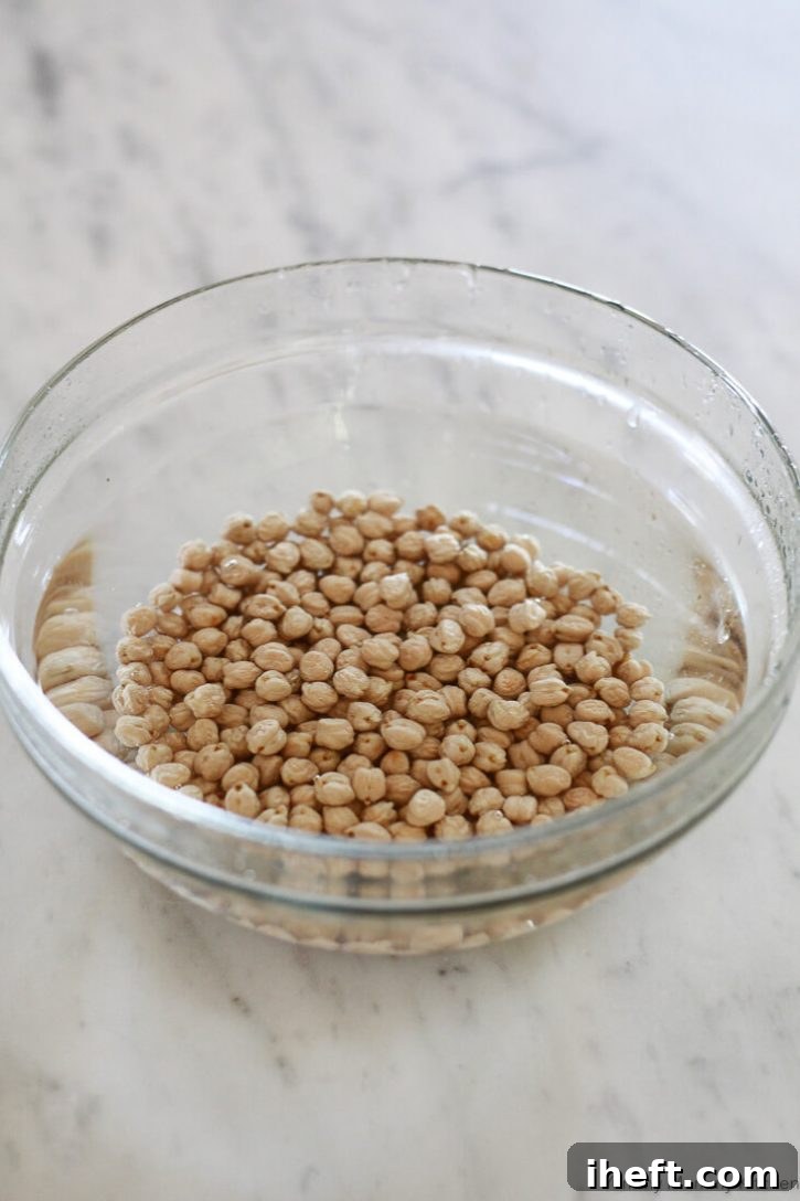 Dried chickpeas soak in a large bowl full of water on a white marble countertop. 