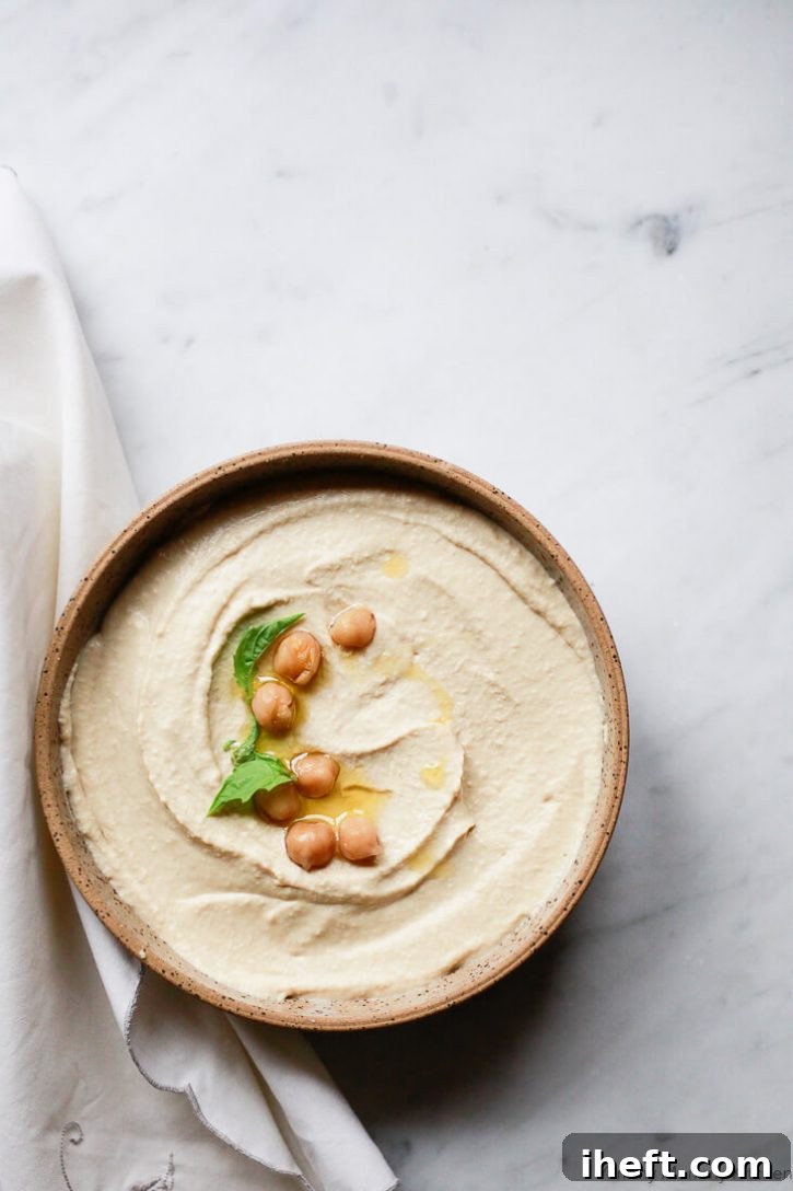 A earthenware bowl filled with homemade hummus sits on a marble countertop. 