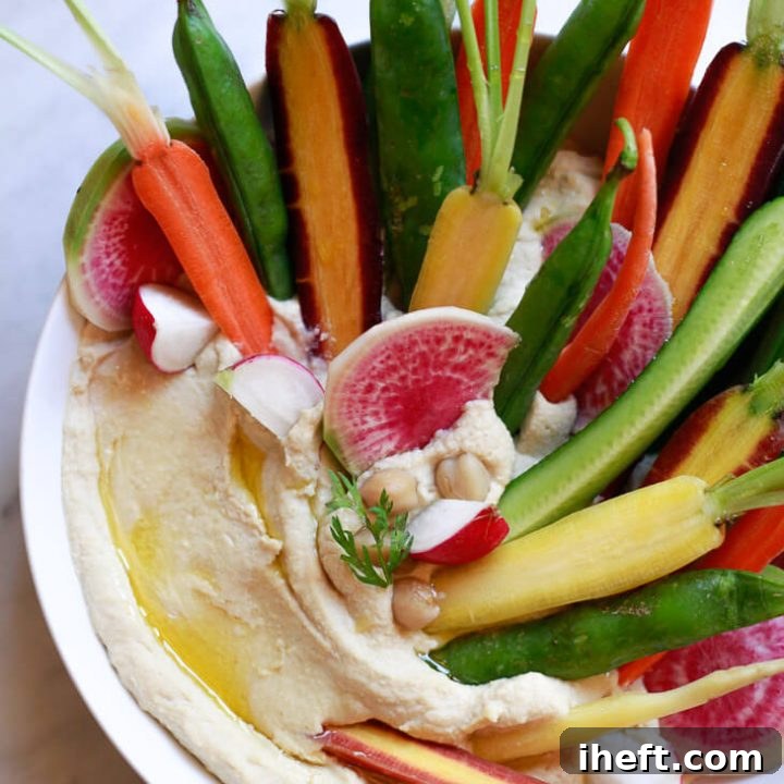 A beautiful bowl of classic homemade hummus topped with colorful carrots, watermelon radish, and cucumber.
