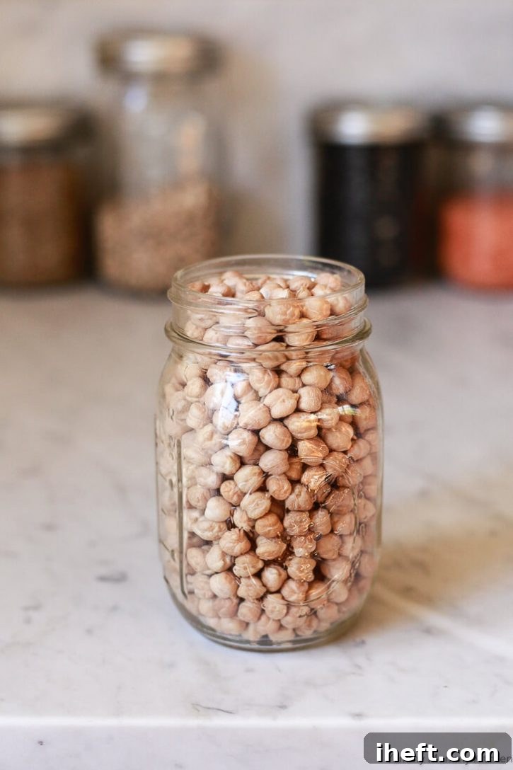 A glass jar of dried chickpeas on a white marble kitchen counter. 