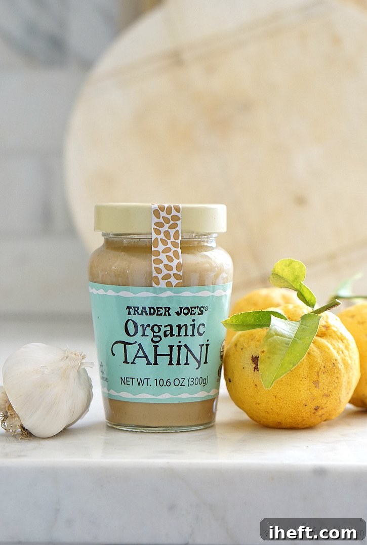 A jar of tahini, a head of garlic, and fresh lemons on a white countertop. 