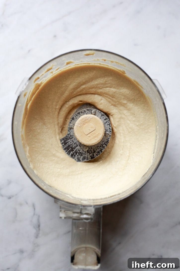 Smooth hummus in a food processor on a white countertop. 