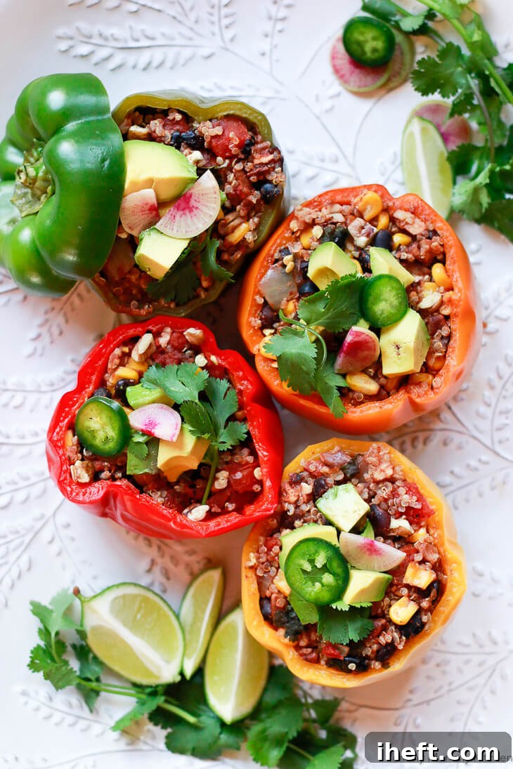 A white platter topped with multi-color vegetarian vegan stuffed bell peppers with quinoa, black beans, and pecans. Peppers are topped with avocado, jalapeno, cilantro, and watermelon radish. 