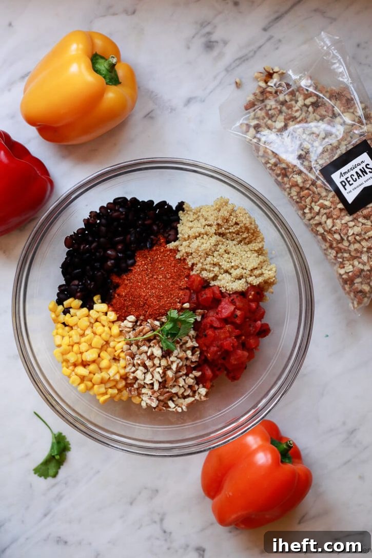 Quinoa, black beans, corn, pecans, taco seasoning, and tomatoes in a glass bowl on a marble countertop. This is the filling ingredients for vegan stuffed bell peppers. 