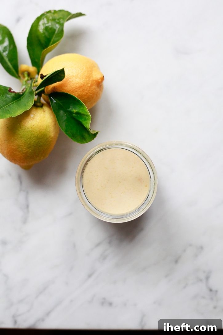 A small, elegant glass jar filled with luscious homemade creamy lemon vinaigrette dressing, resting gracefully on a pristine white marble kitchen countertop, ready to elevate any meal.