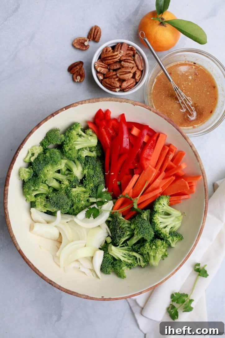 The ingredients for stir fry vegetables are chopped and ready to cook. They sit in a white bowl with a small dish of orange stir fry sauce on the side.