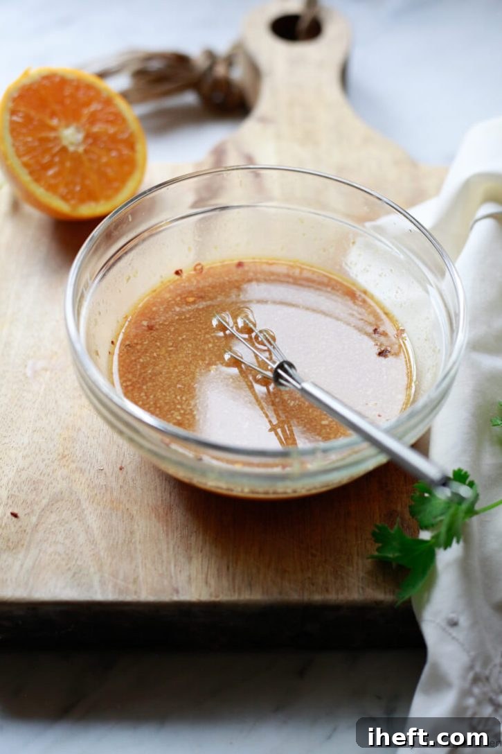 Homemade orange stir fry sauce in a small glass bowl with small whisk on a cutting board.
