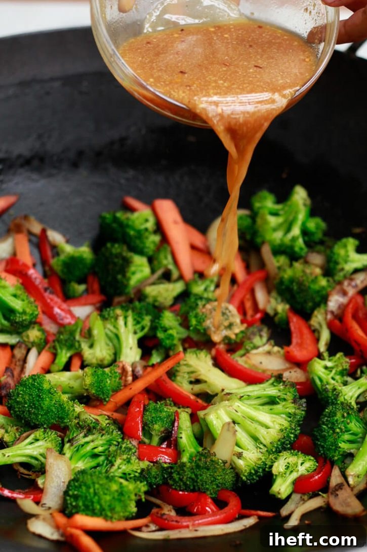 Stir fry sauce gets poured over stir fry vegetables in a black wok.