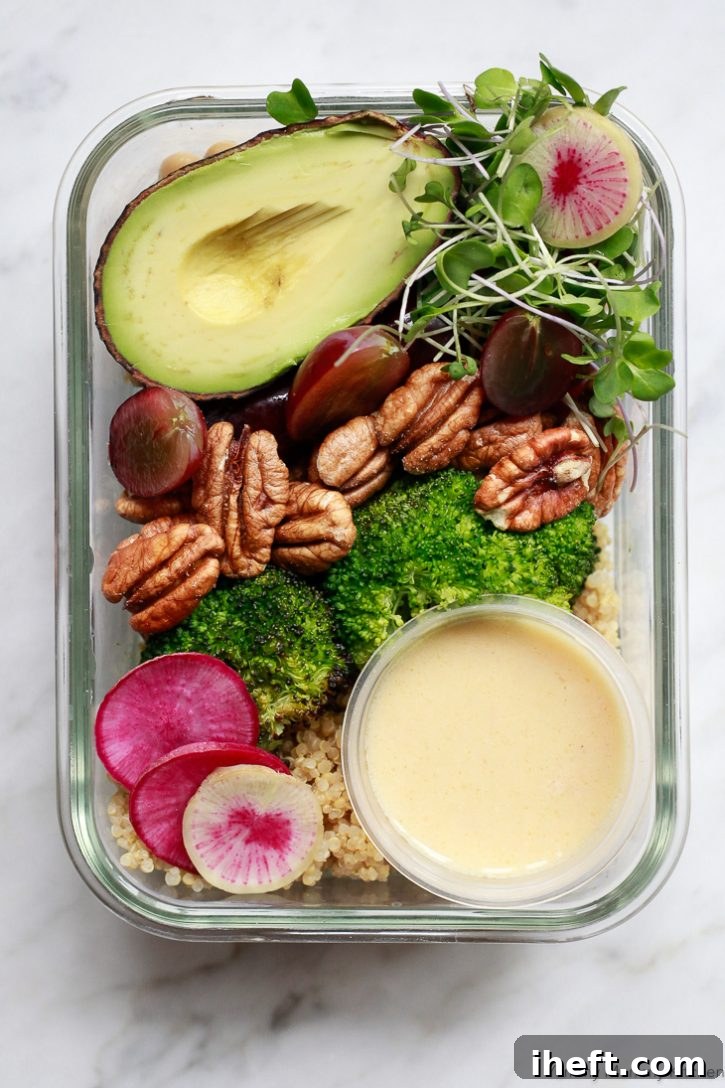 A colorful vegan meal prep container filled with quinoa, roasted broccoli, grapes, avocado, and pecans, drizzled with lemon vinaigrette.