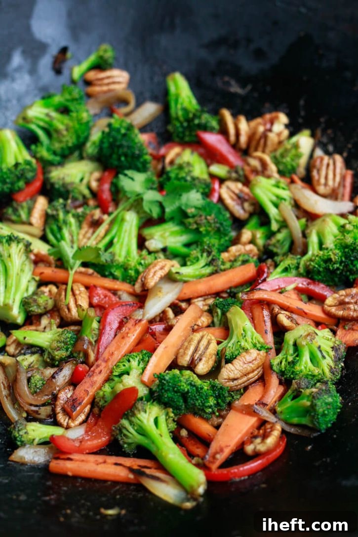 A black wok filled with a vibrant array of stir-fry vegetables and pecans, coated in a savory sauce.