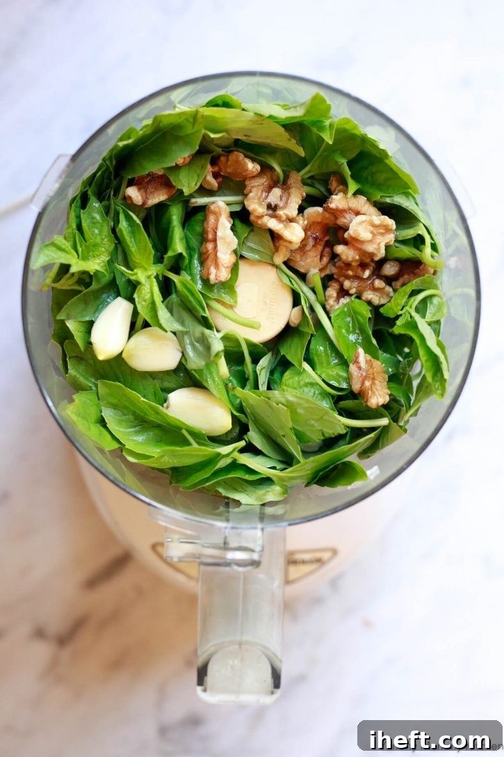 Fresh basil leaves, whole garlic cloves, and walnuts halves in a food processor to make vegan pesto sauce. 