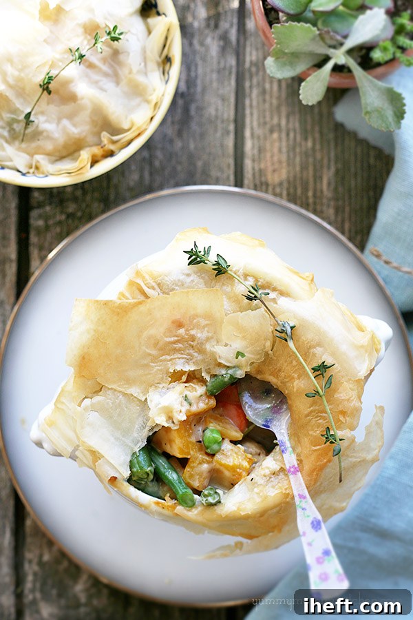 Mini pot pie featuring a golden-brown phyllo top, revealing a rich, colorful filling of peas, green beans, and butternut squash.