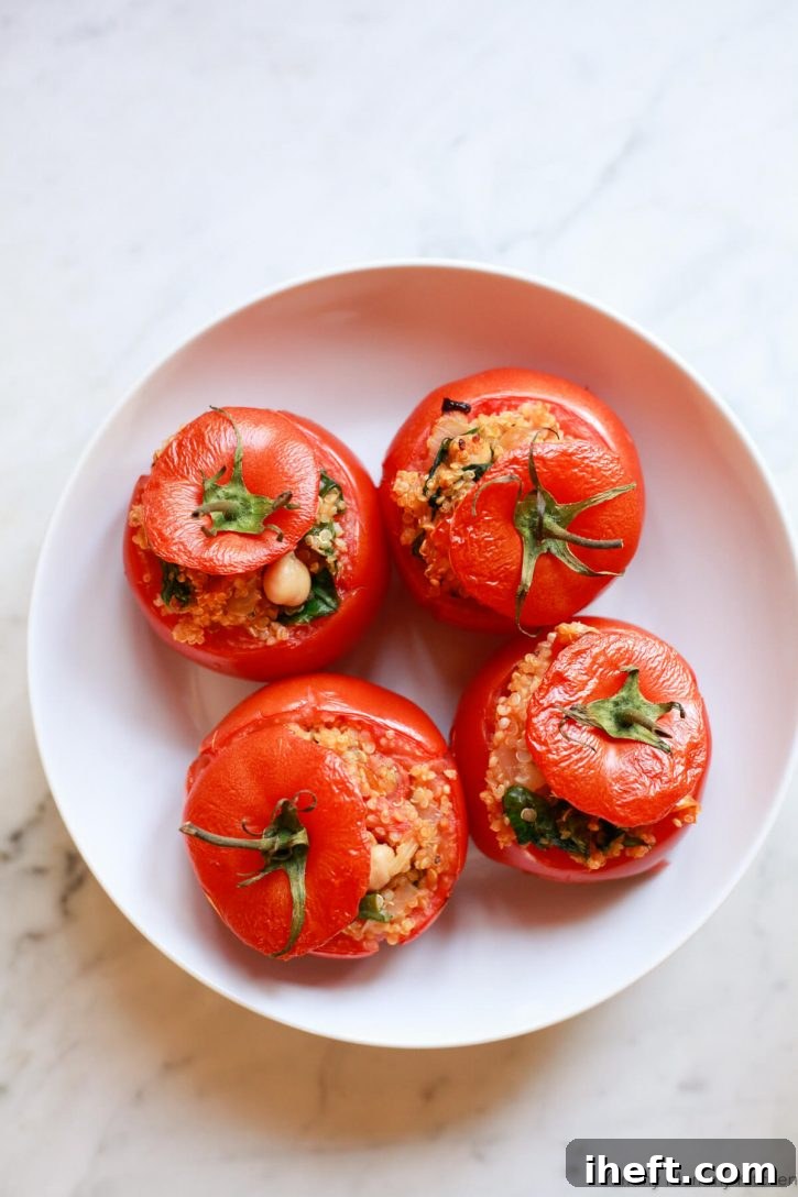 A white bowl filled with four vegetarian stuffed baked tomatoes filled with quinoa, chickpeas, and spinach. 