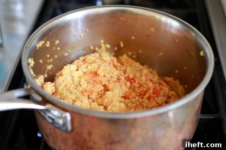 Quinoa cooks in a saucepan with tomato pulp to fill stuffed baked tomatoes. 