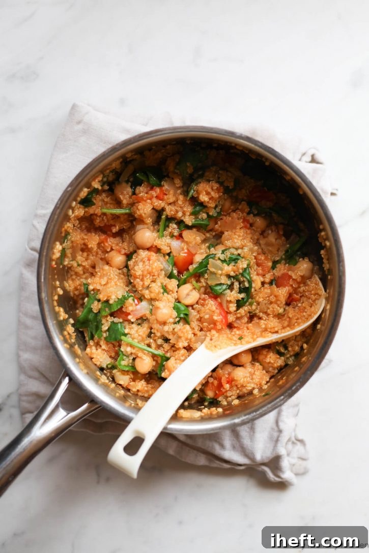 A saucepan with the filling for stuffed tomatoes sits on a white marble countertop. The filling is made with quinoa, chickpeas, tomatoes, and spinach. 