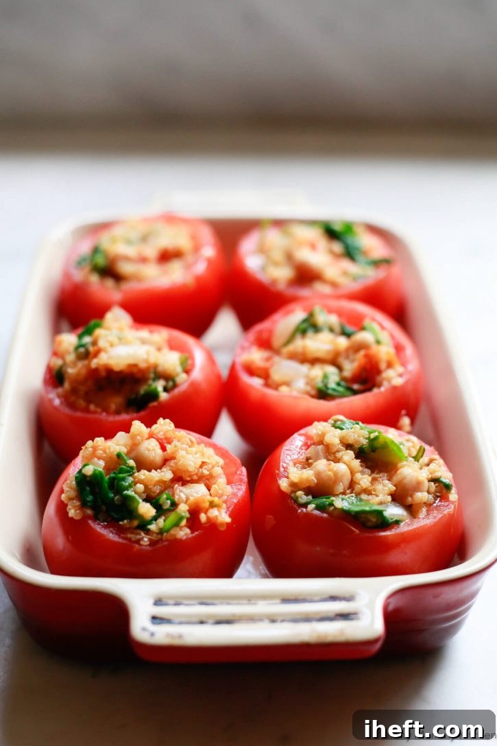 Raw tomatoes filled with quinoa sit on a casserole dish before being baked in the oven. 