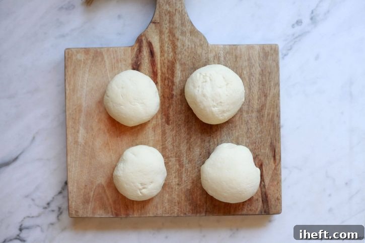 Four small balls of pizza dough resting on a wooden cutting board. 