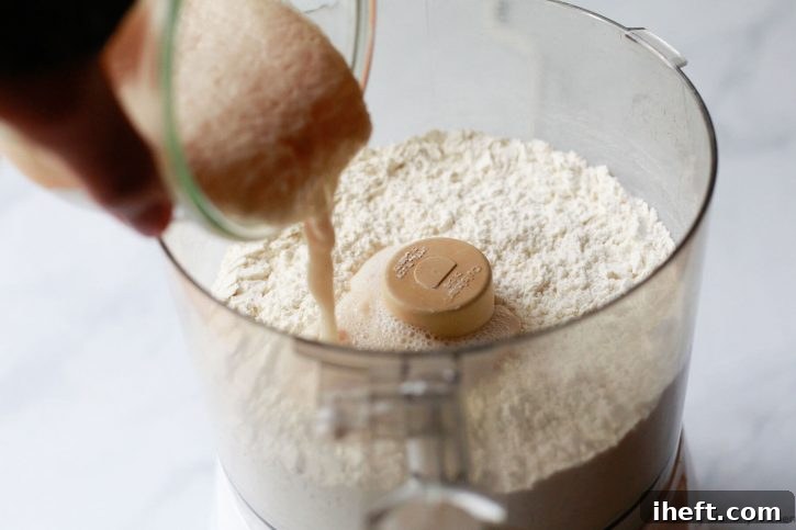Proofed yeast and water is poured into flour in a food processor.