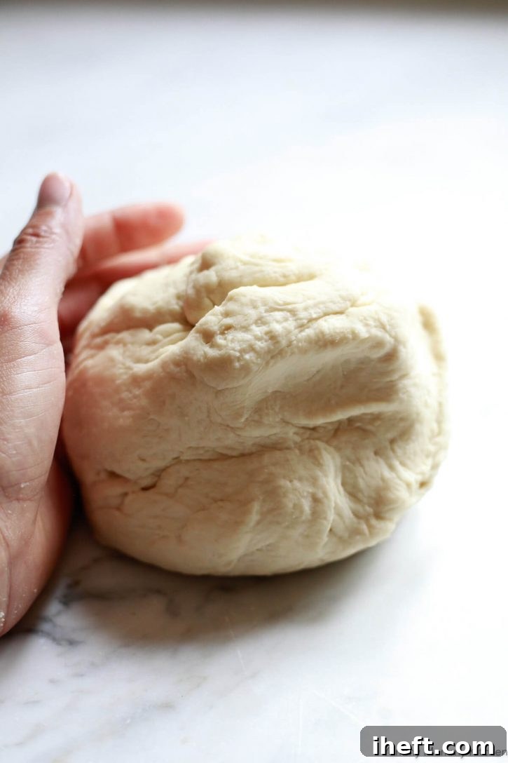 A hand kneads a fresh ball of homemade pizza dough on a marble countertop. 
