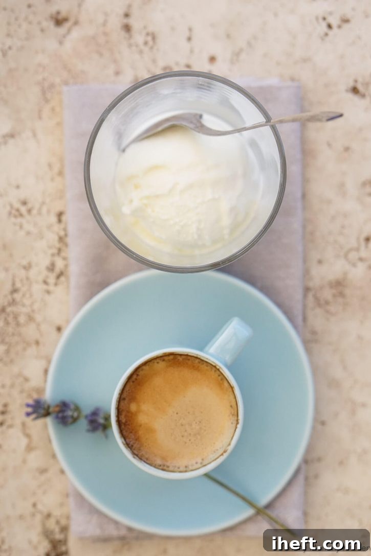 A single scoop of creamy vanilla ice cream sits invitingly at the bottom of a clear glass, positioned right next to a small cup holding a fresh shot of dark espresso, showcasing the two primary components ready to be combined for an Italian coffee dessert.