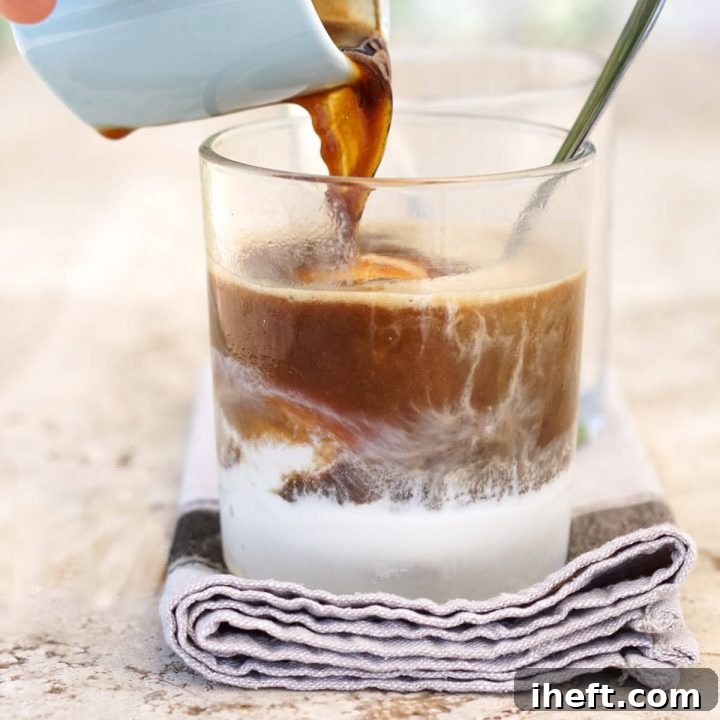 A hand expertly pours a shot of steaming espresso over a scoop of creamy vanilla ice cream, creating the iconic Italian affogato dessert.