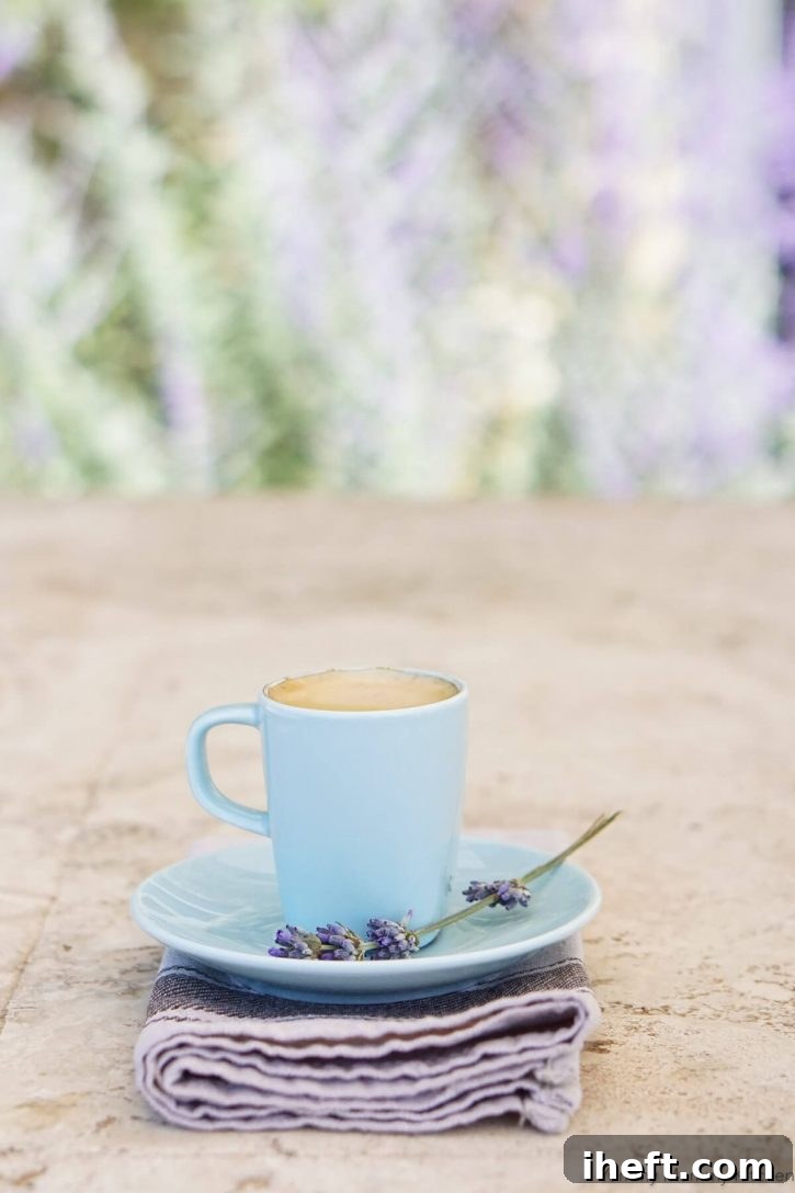A small blue mug filled with a lavender latte sits on a saucer with fresh lavender sprig.