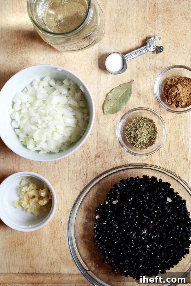 Ingredients for Instant Pot black beans on a cutting board include dried black beans, onion, garlic, oregano, bay leaf, cumin, salt, and water. 