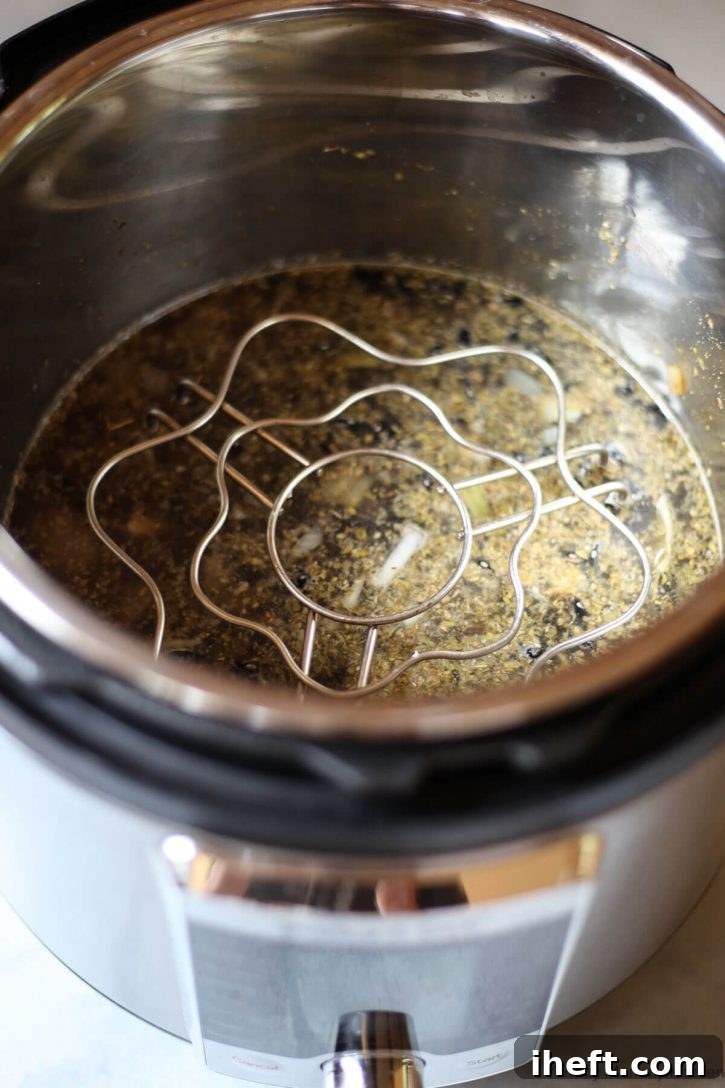 An Instant Pot electric pressure cooker with ingredients for black beans in the bottom and a trivet on top for pot-in-pot beans and rice. 