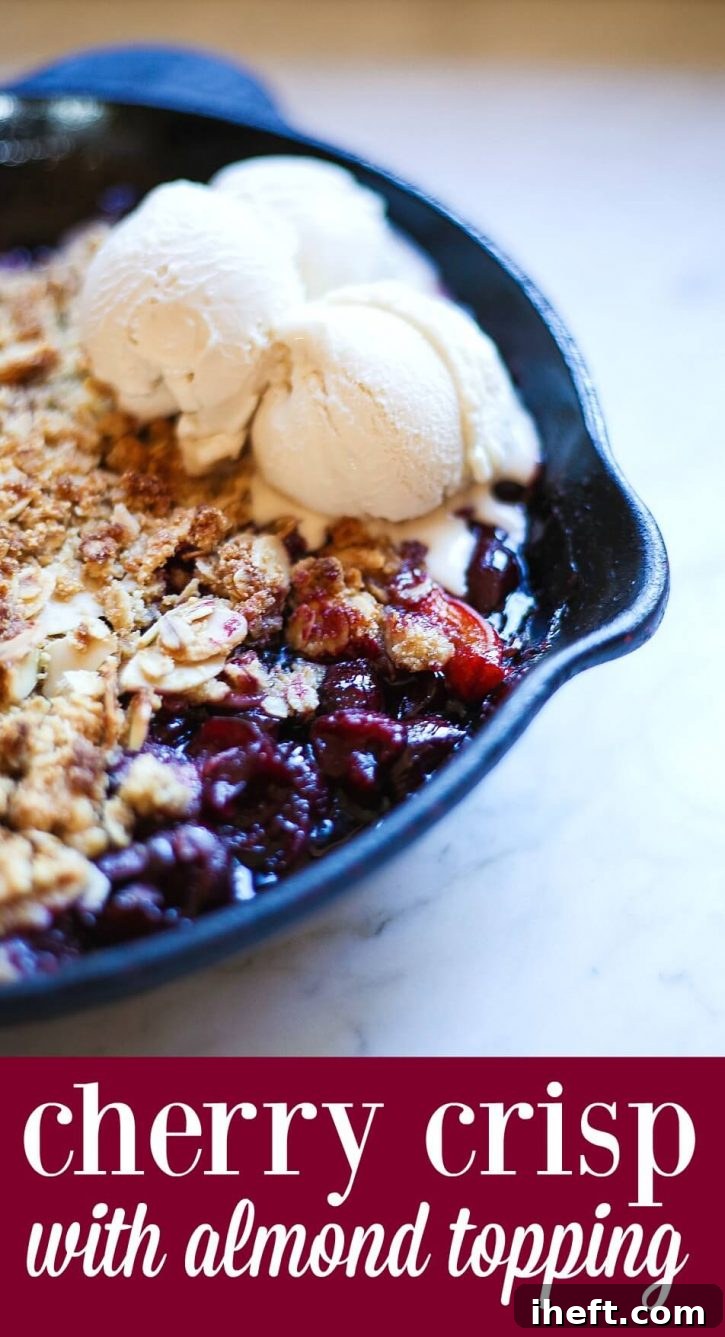 A close-up of a cherry crisp made with fresh cherries and a gluten free almond oat crumble topping. This cherry crisp is made in a skillet and topped with scoops of vanilla ice cream. 
