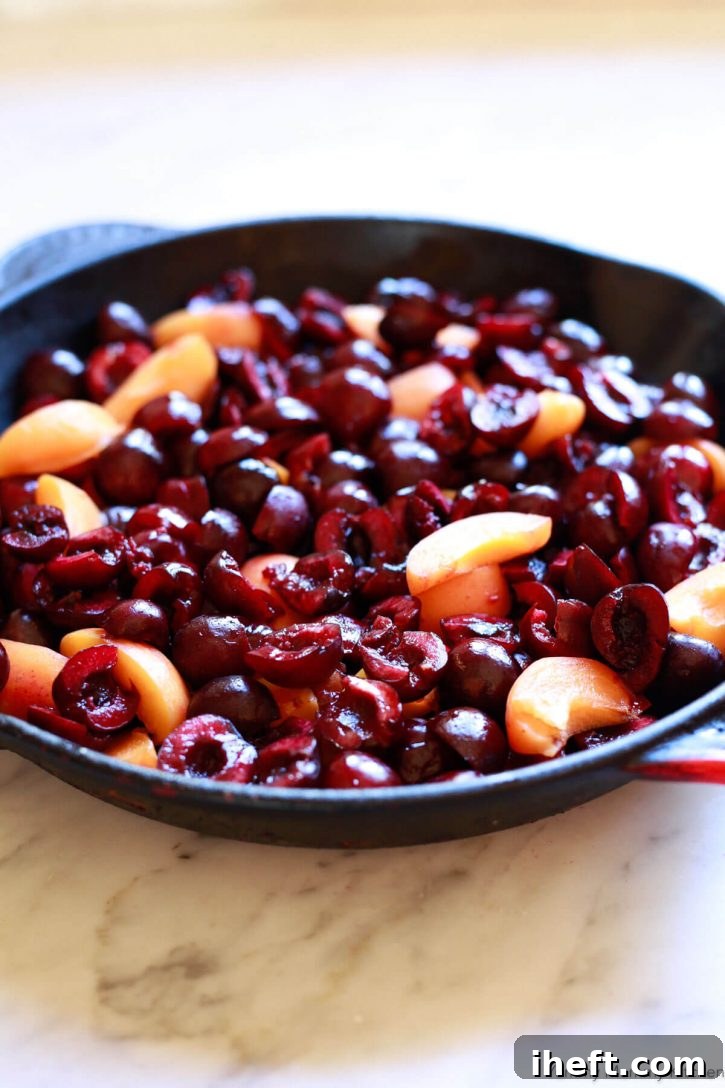 Fresh pitted cherry halved and apricot slices in a cast iron skillet on a white marble countertop. 