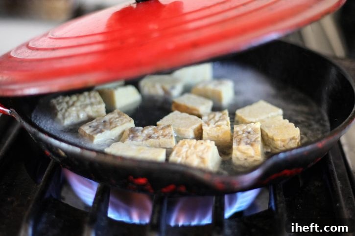 Cubed tempeh steams in a skillet.