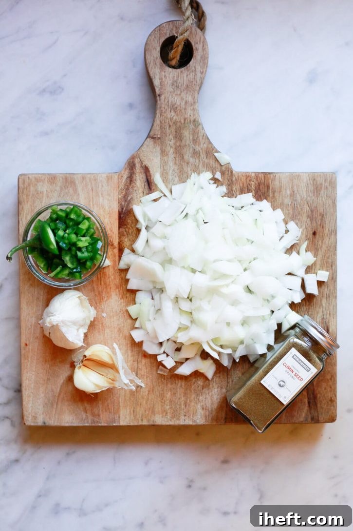 A cutting board with the ingredients for Mexican pinto beans. Chopped onion, cumin, garlic, and jalapeno. 